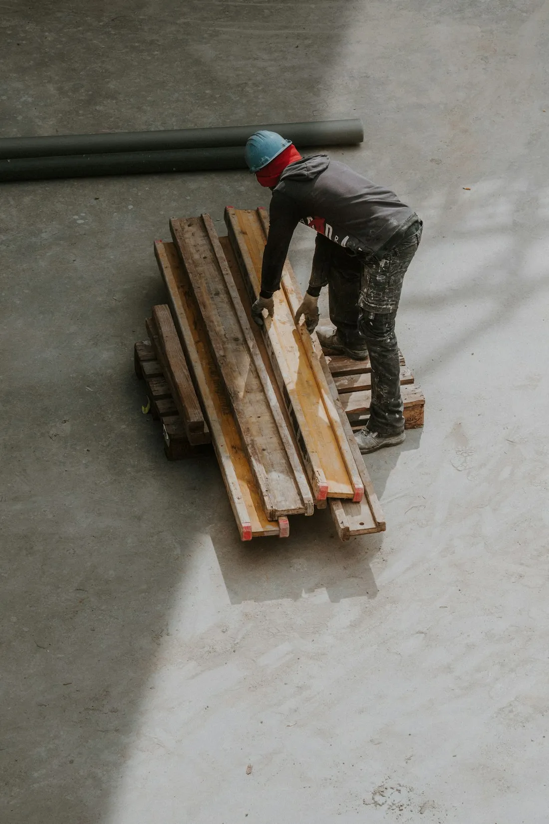 Imagem ilustrativa: trabalhador de capacete organizando madeiras na obra